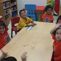 Four children sitting at a table, one child raising a hand