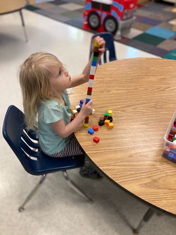 Child sitting at a table, holding a tall stack of colorful building blocks