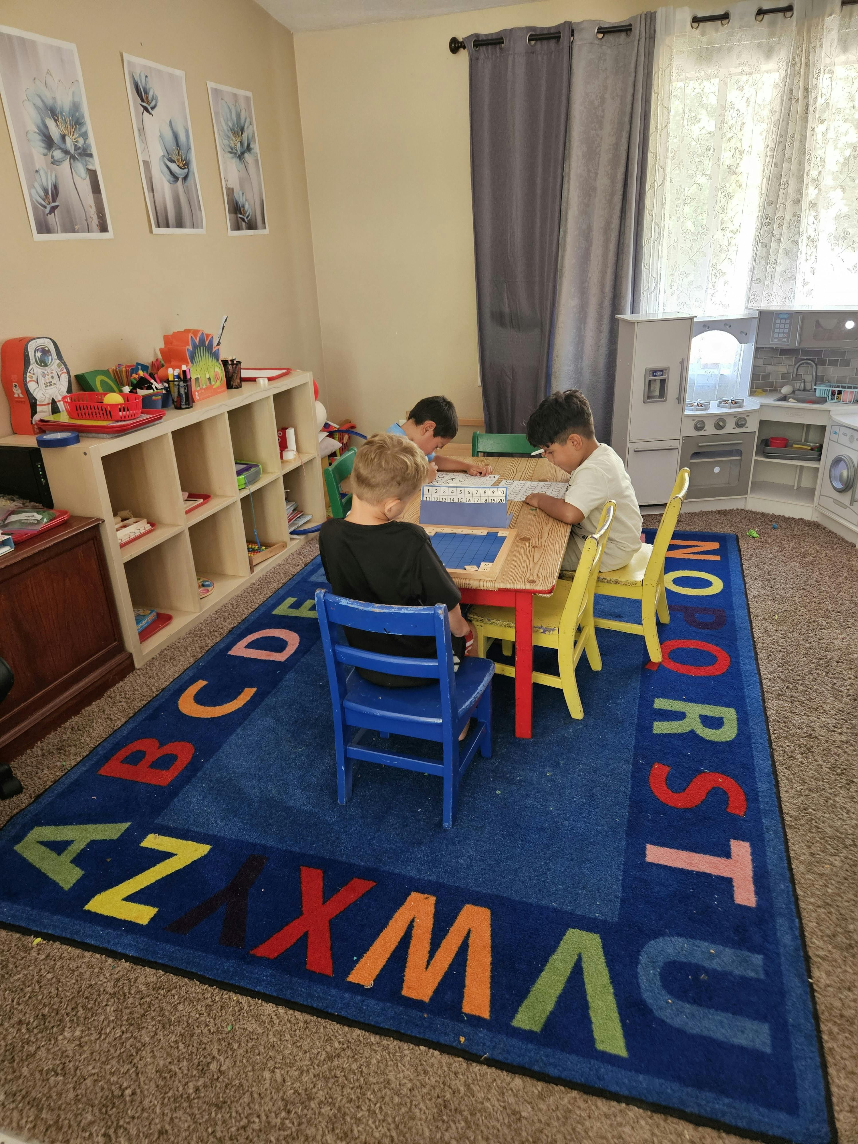 Three children sitting at a small table in a room with an alphabet rug