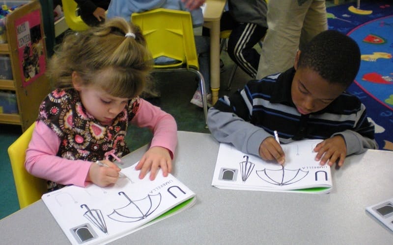 Two children drawing umbrellas and the letter U