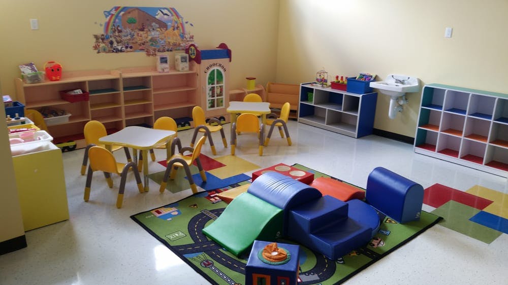 Playroom with small tables, chairs, shelves, and soft play equipment