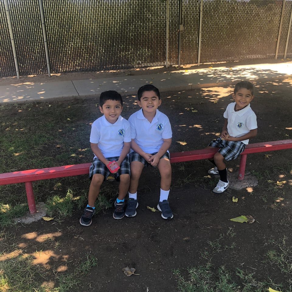 Three children in uniform sitting on a red bench outdoors