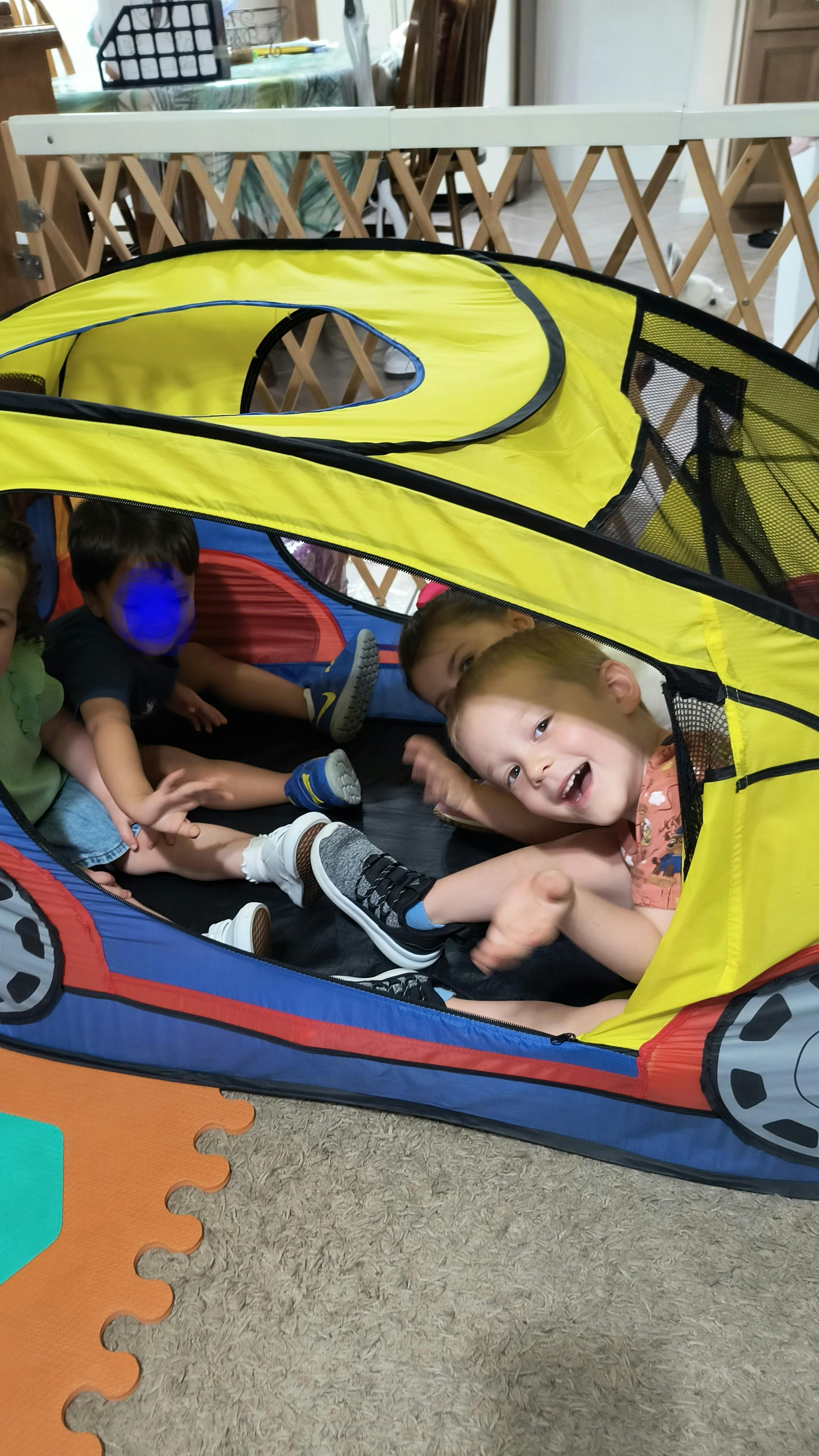 Three children playing inside a yellow car-shaped play tent