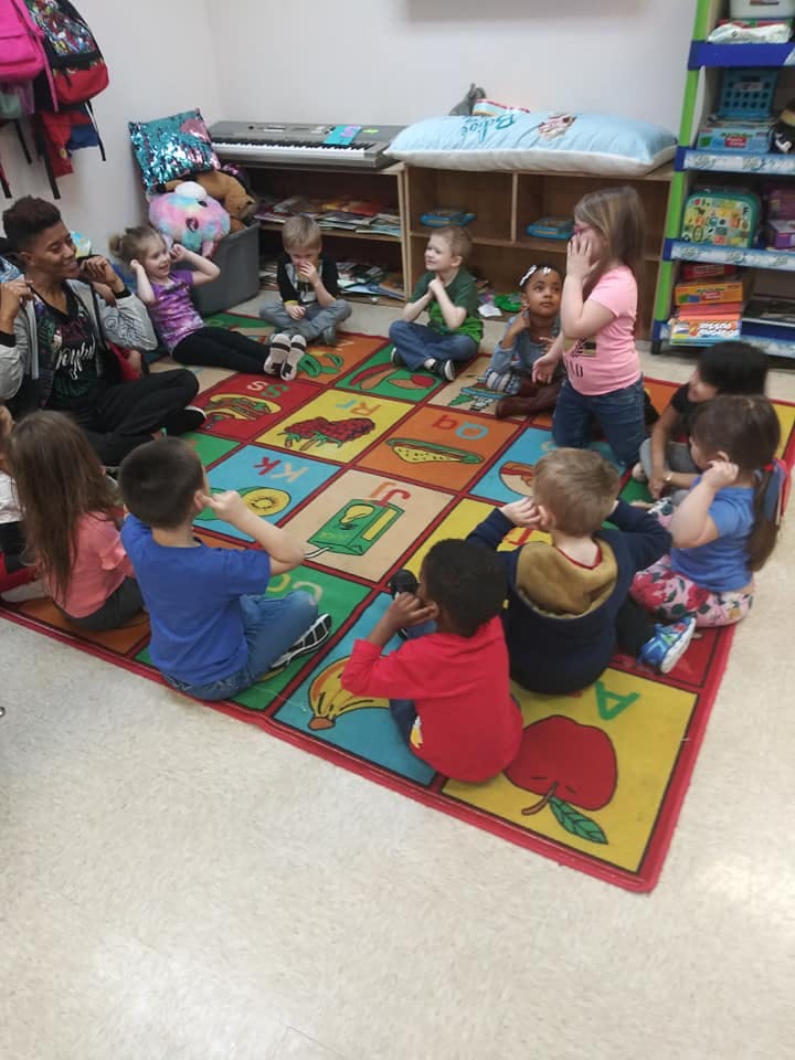 Adult and children sitting on a colorful rug in a classroom