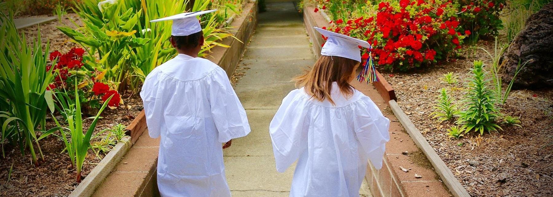 Two people in graduation gowns and caps walking away