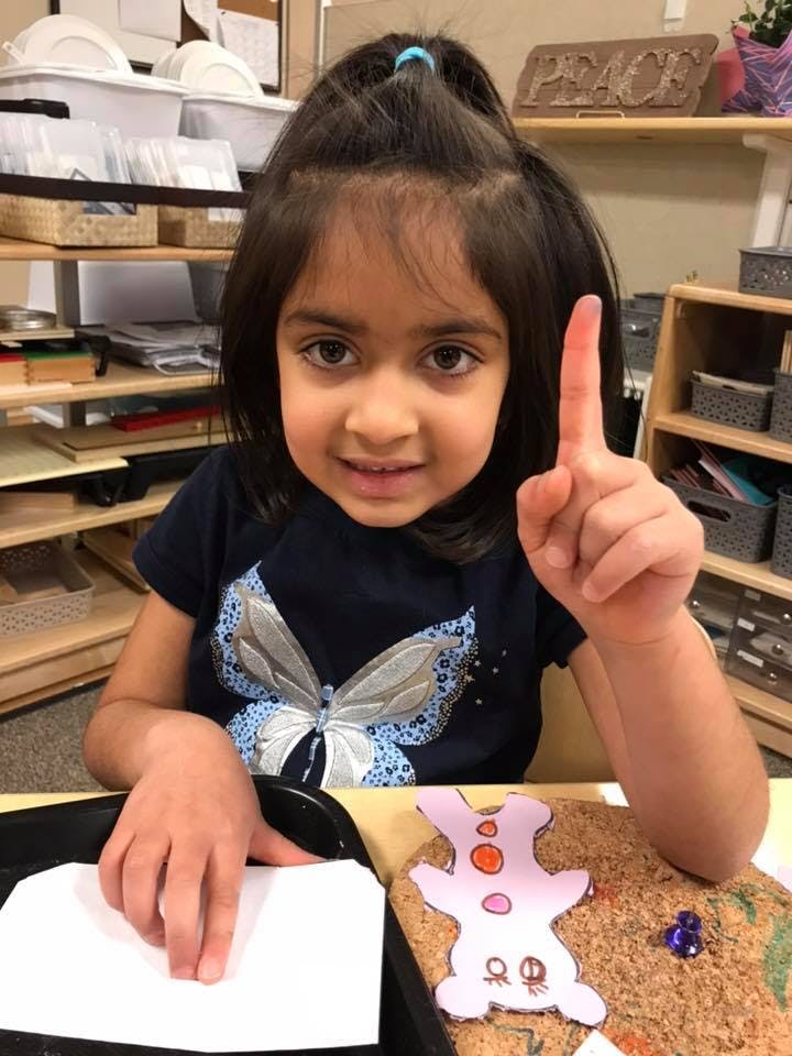 Child in a classroom raising a finger