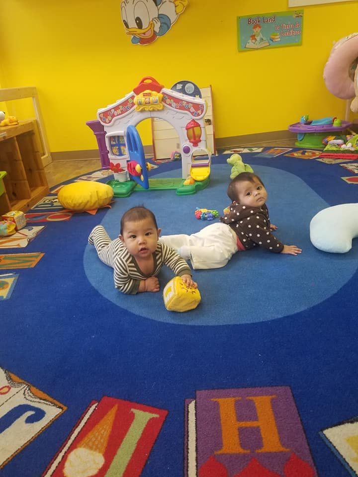 Two children crawling on a blue rug in a playroom