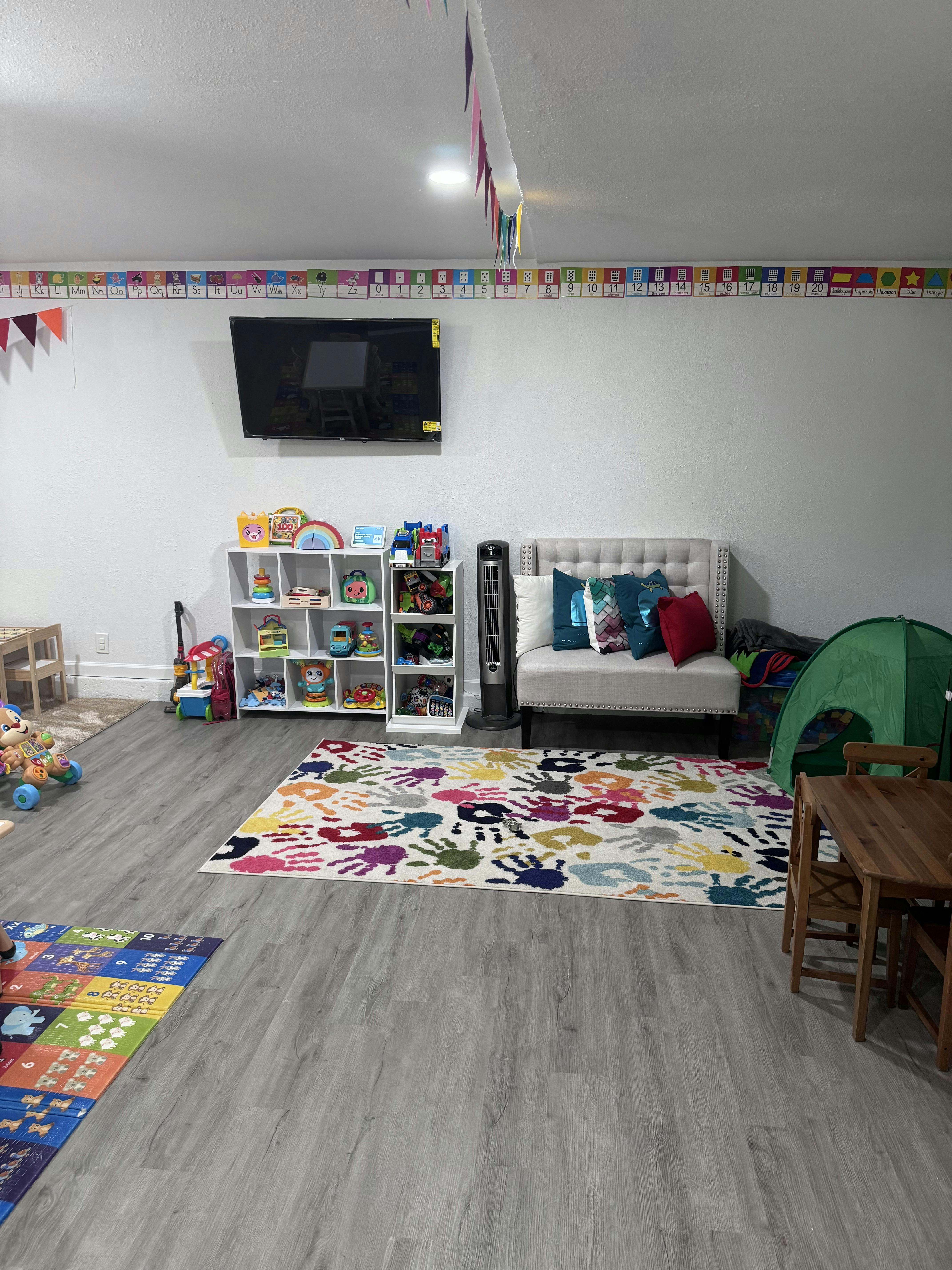 Playroom with a TV, sofa, toy shelves, and a colorful rug