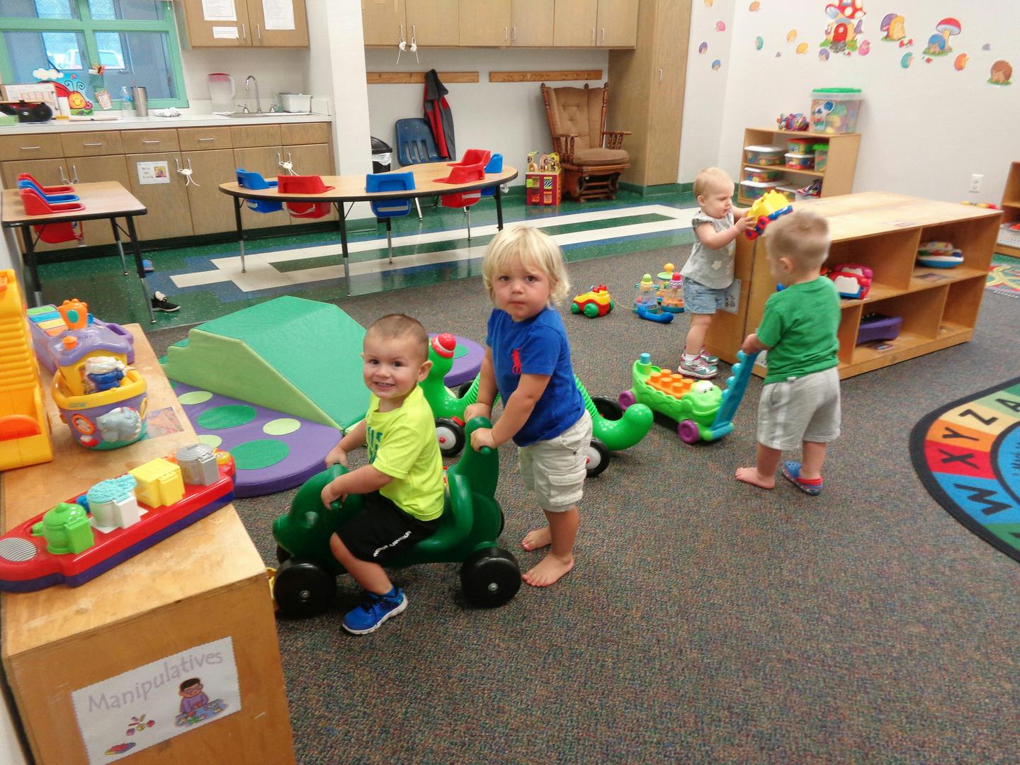 Children playing with ride-on toys in a classroom