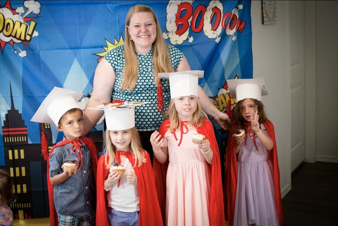 Person with four children in graduation caps and red capes holding cupcakes