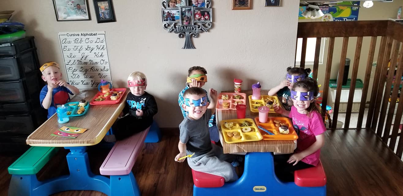 Children with painted faces sitting at small tables with food trays