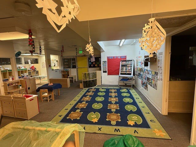 A classroom with a turtle-themed rug, small tables and chairs, and paper decorations