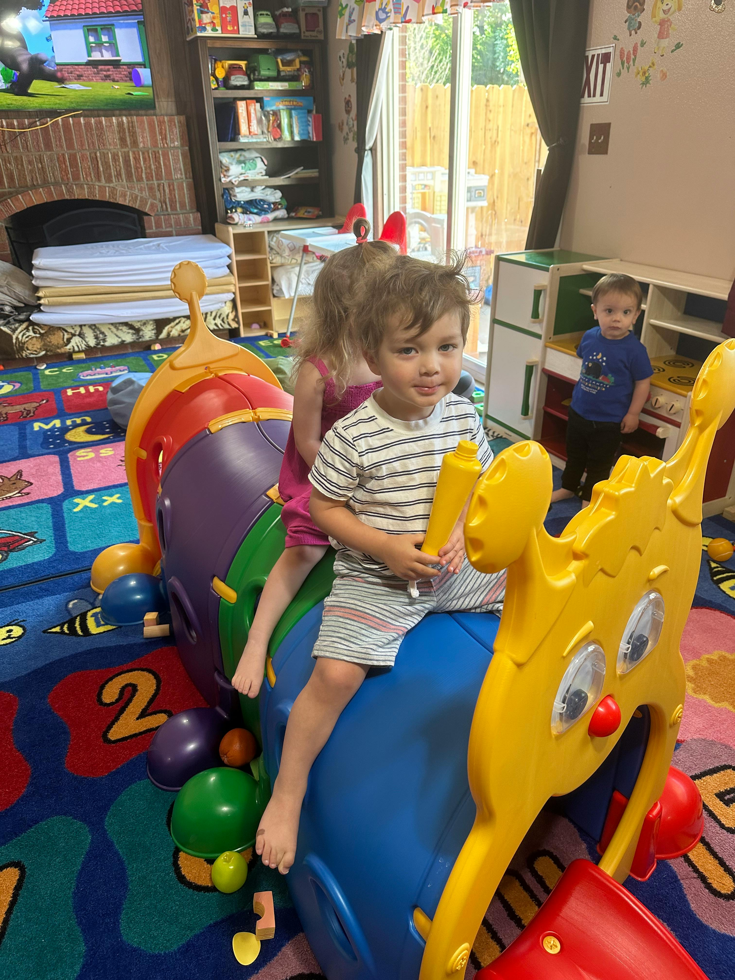 Child sitting on a blue and yellow toy, another child behind