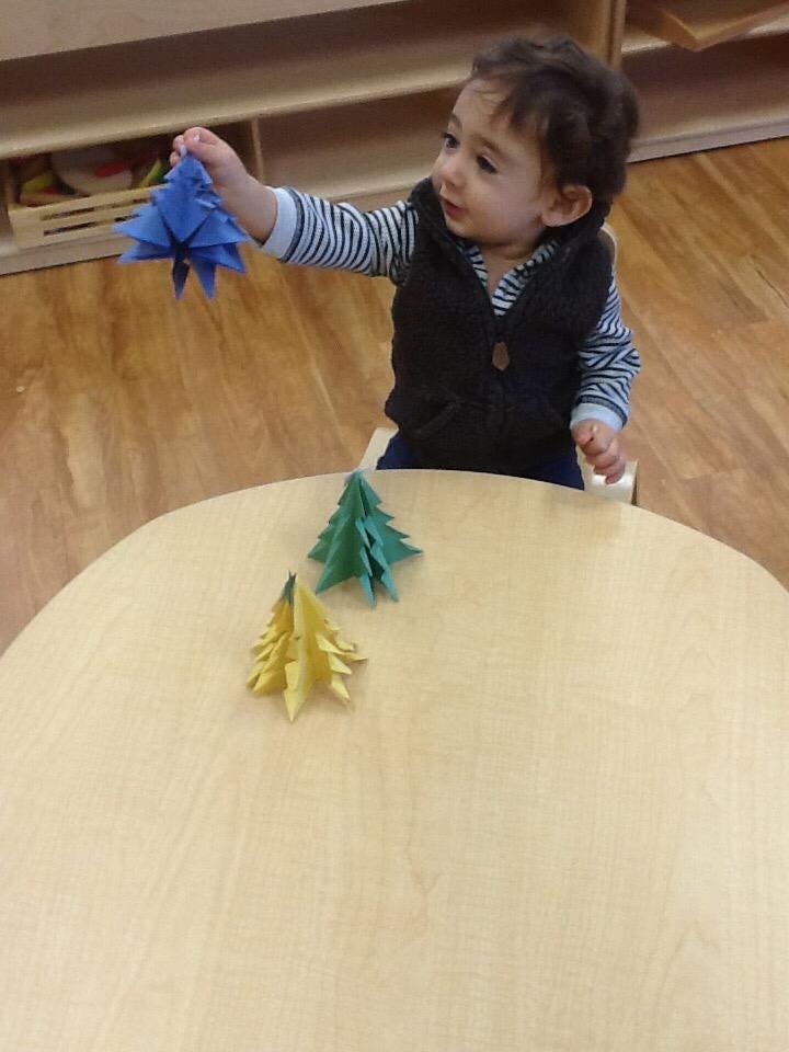 Child holding a blue paper tree over a table with two other paper trees