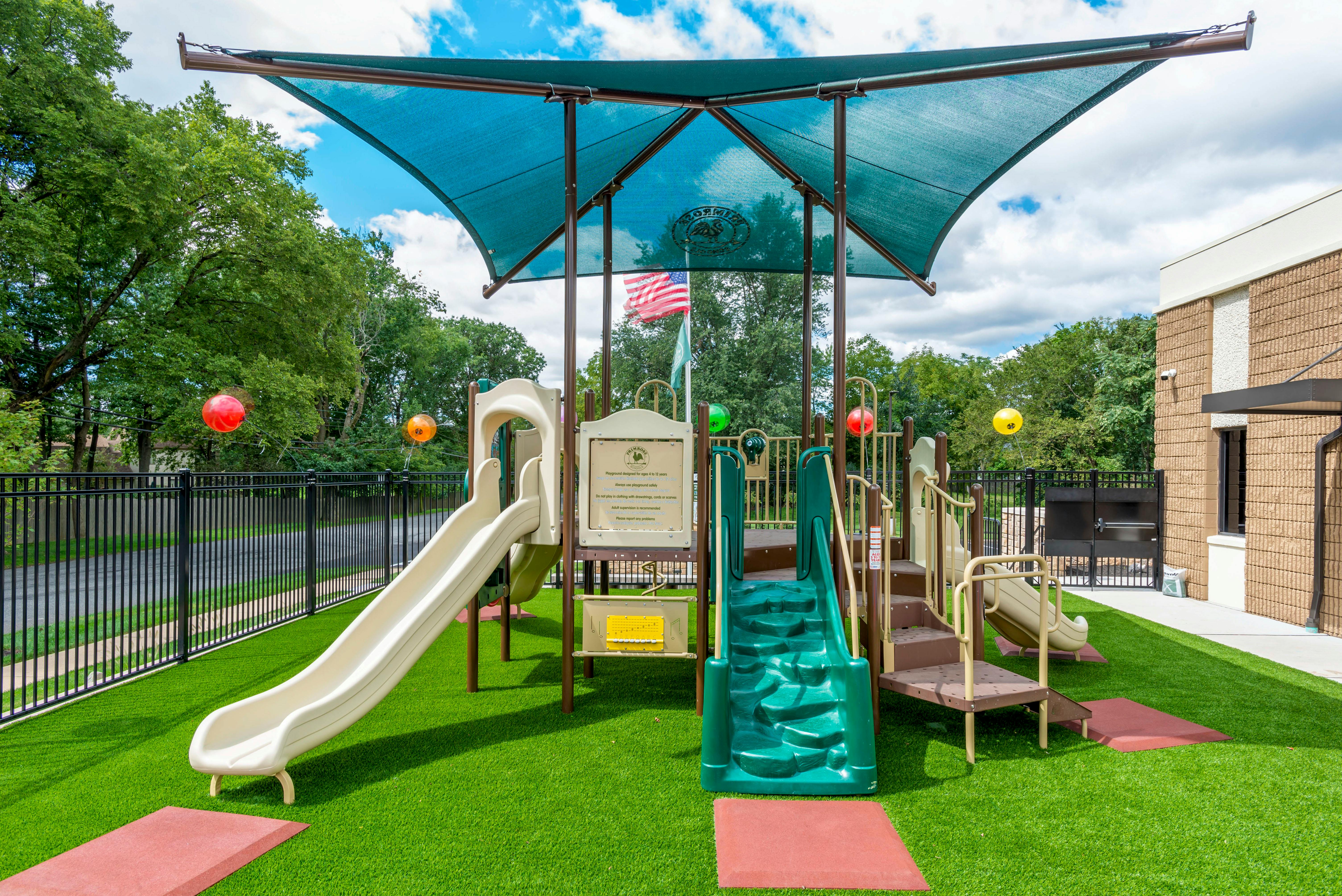 A playground with slides, stairs, a climbing ramp, and a blue canopy shade