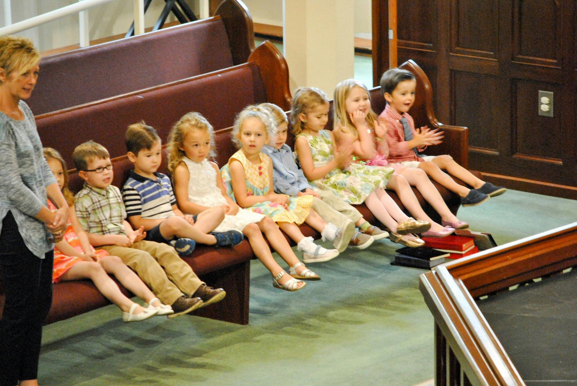 Adult person standing next to a bench with several children sitting on it