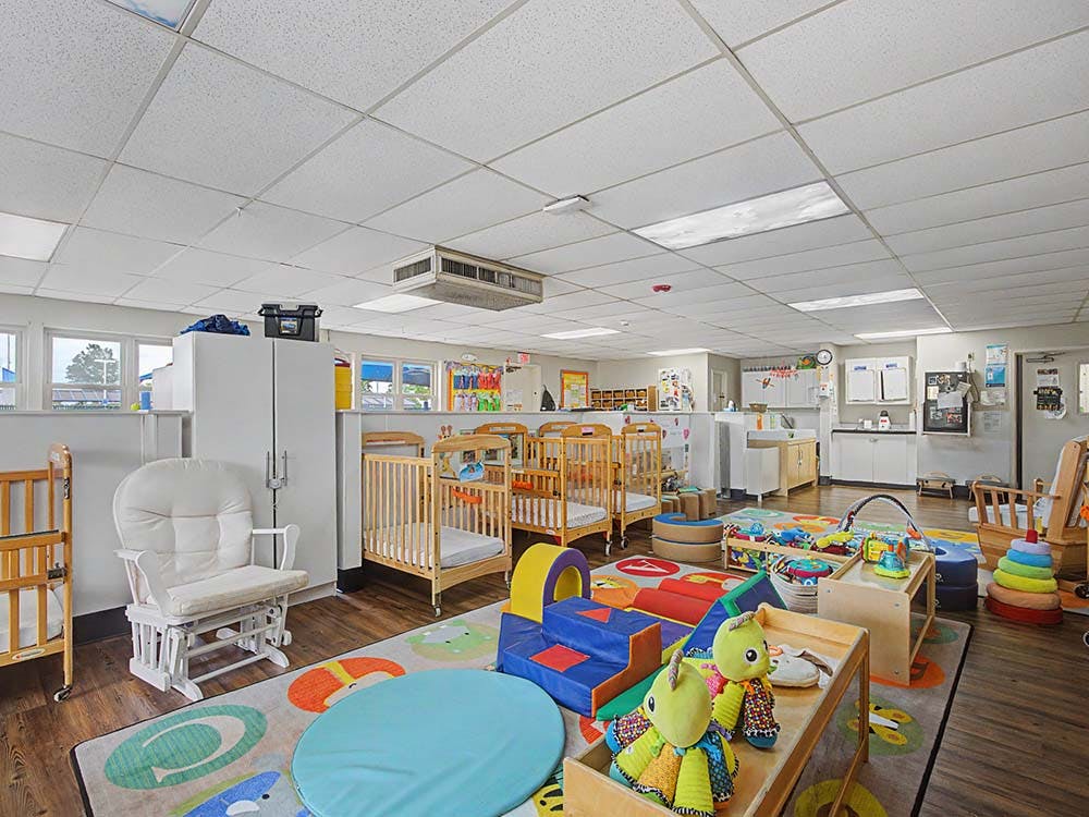 An empty nursery room with cribs, play mats, and a rocking chair