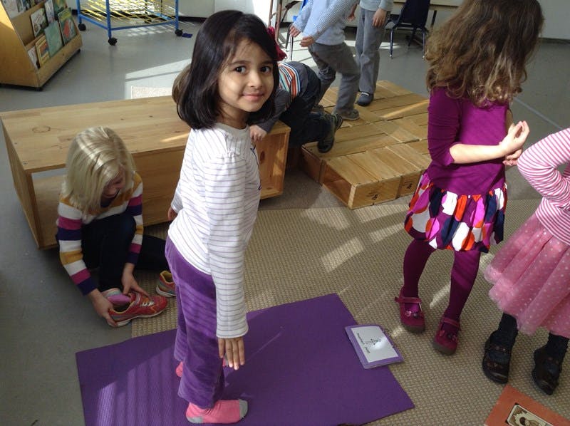 Child standing on a purple mat, another child tying a shoe