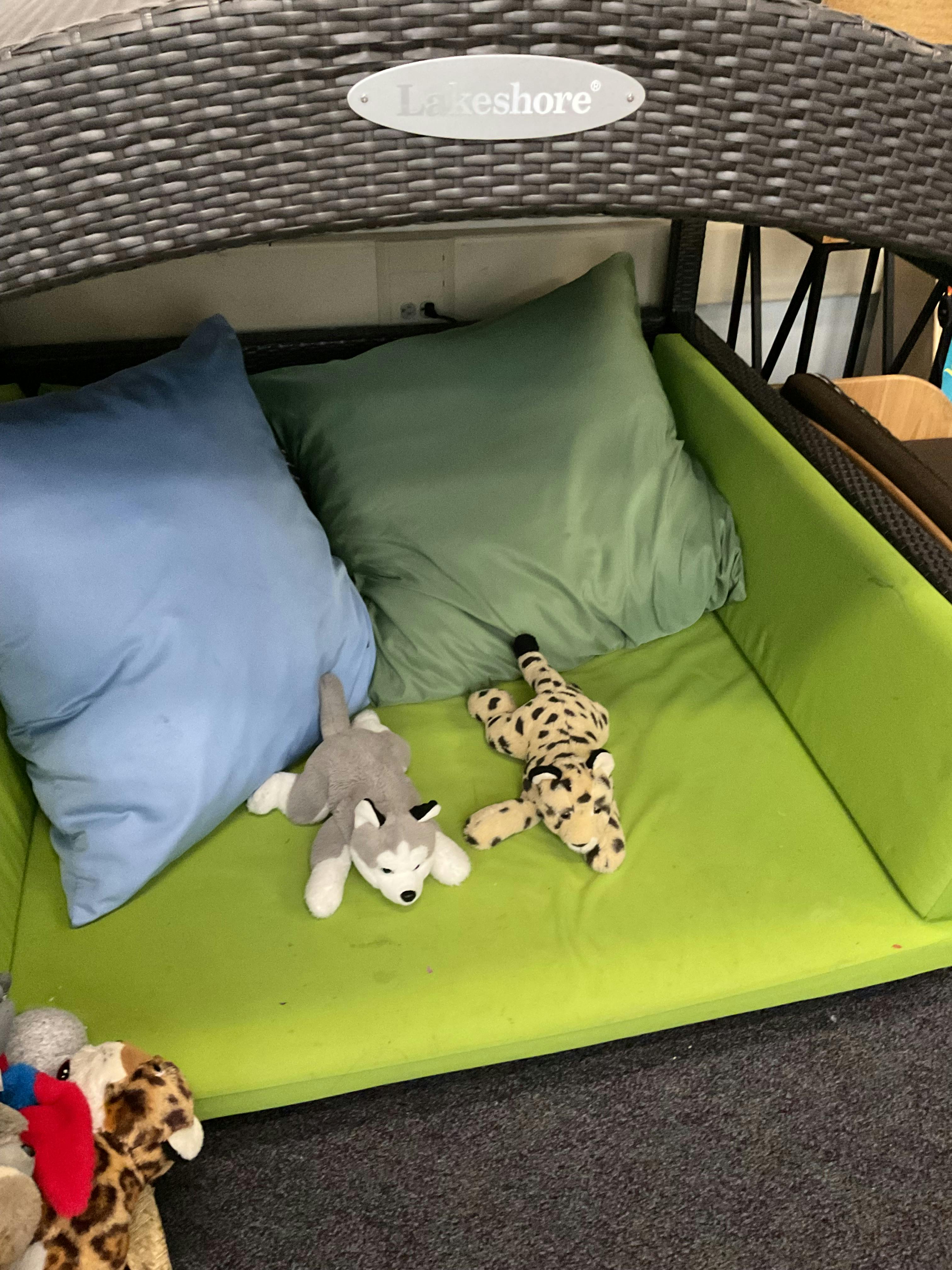 Two stuffed animals on a green cushion with pillows
