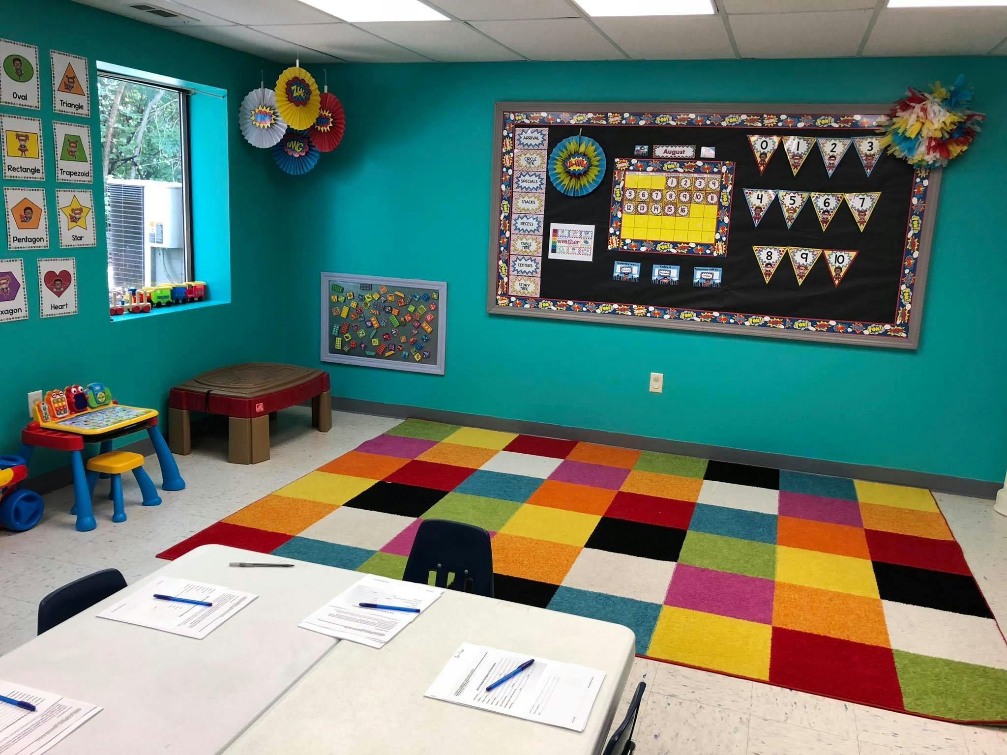 Classroom with colorful rug, bulletin board, and small tables