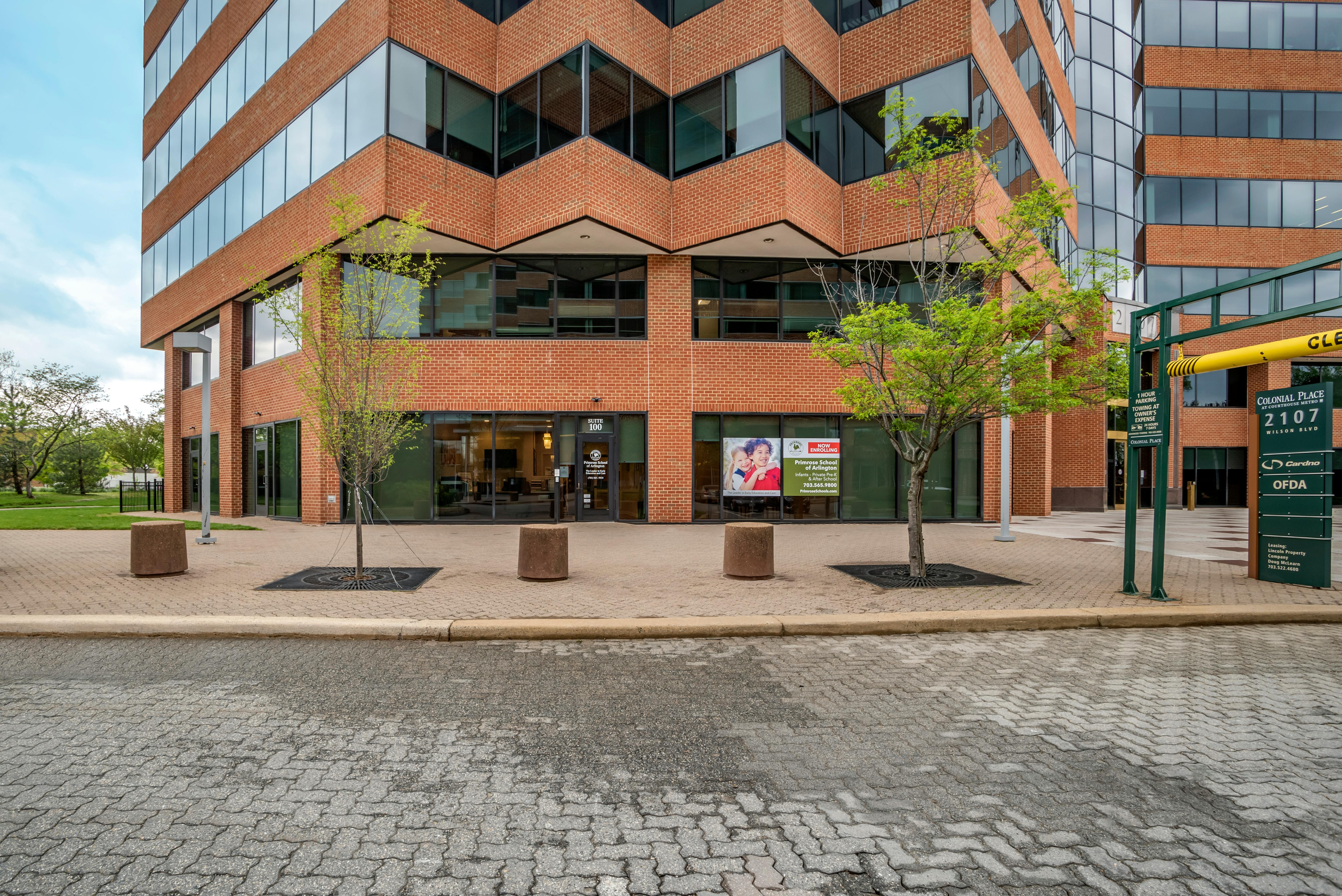 Brick building with many windows, trees, sidewalk, and a sign for Primrose School