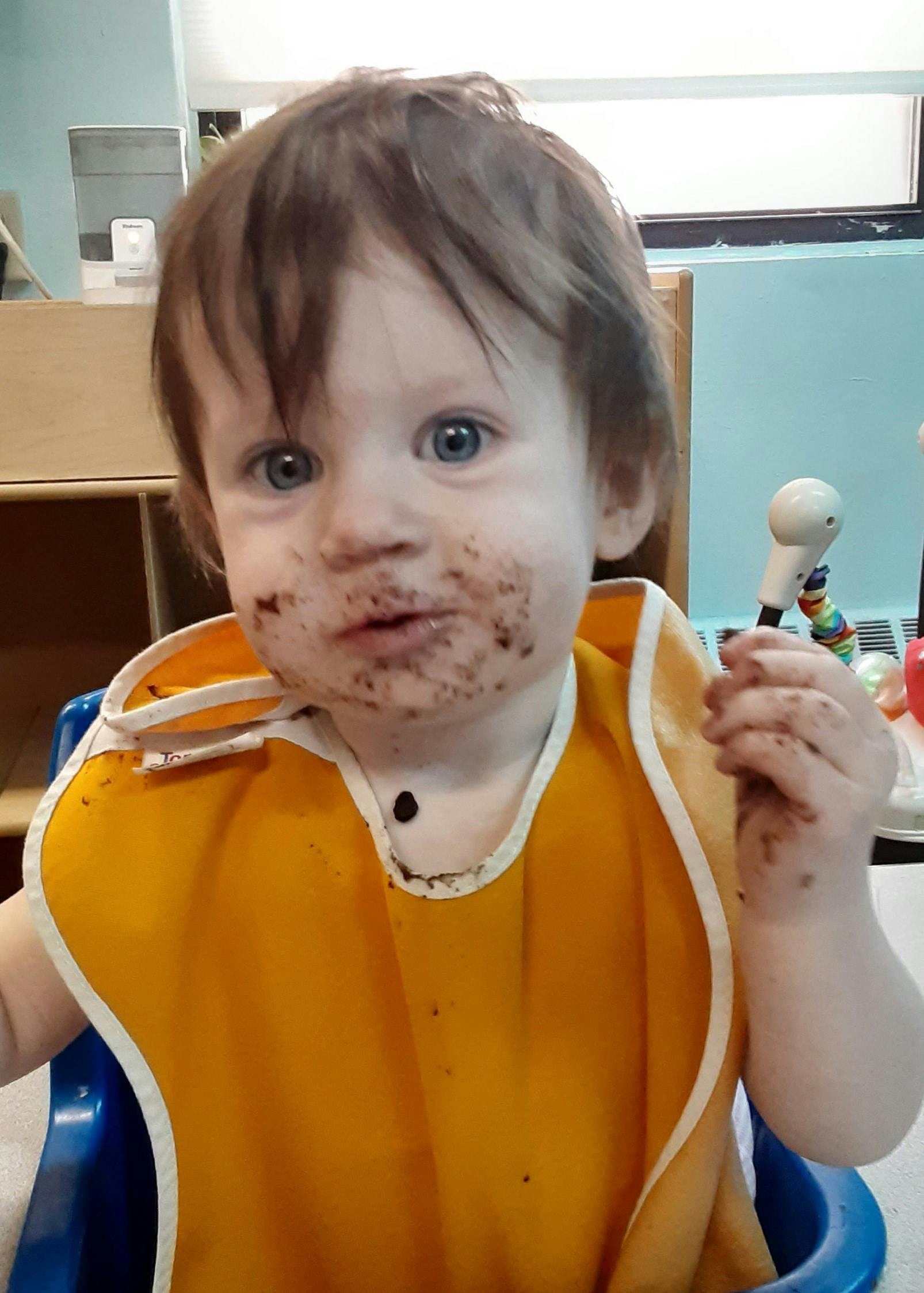 Child in a high chair with a bib and food on their face