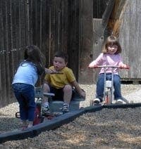 Three children playing on outdoor riding toys