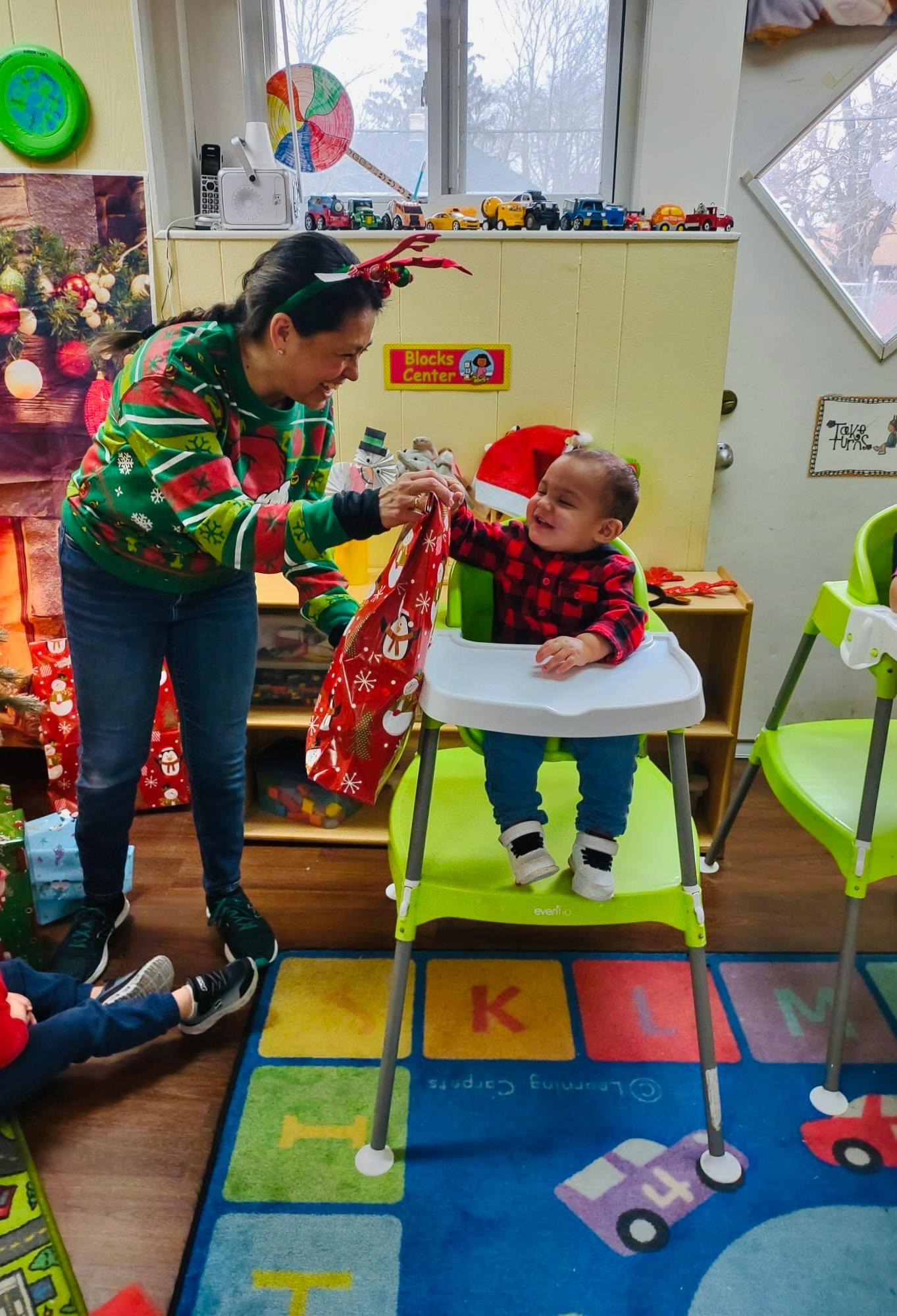 Person in holiday sweater giving a gift bag to a child in a high chair