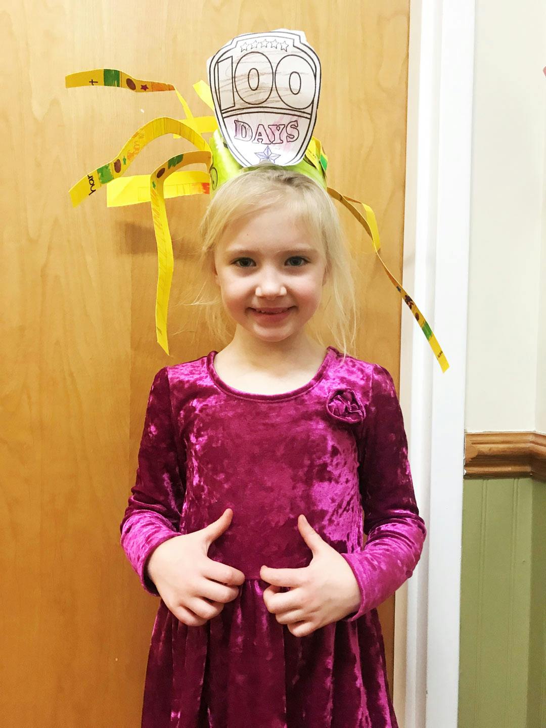 Child wearing a paper crown with "100 Days" written on it