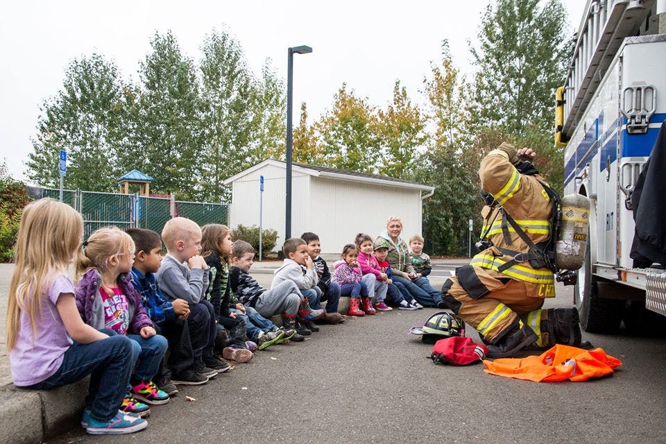 Firefighter kneeling in front of children sitting on a curb