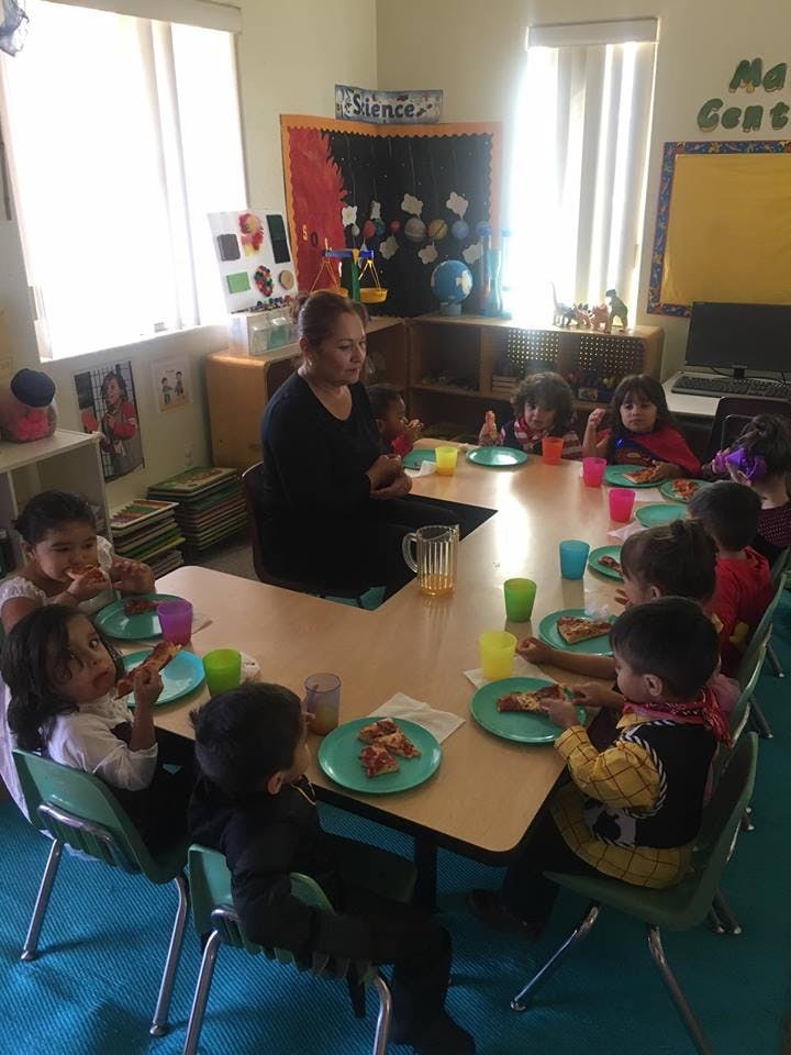 Adult and children sitting at a table eating in a classroom