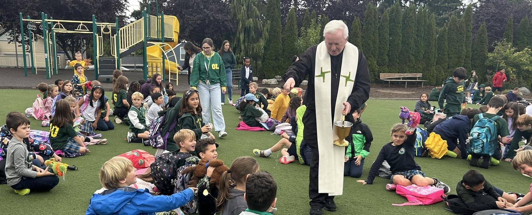 Priest blessing children with holy water during an outdoor event
