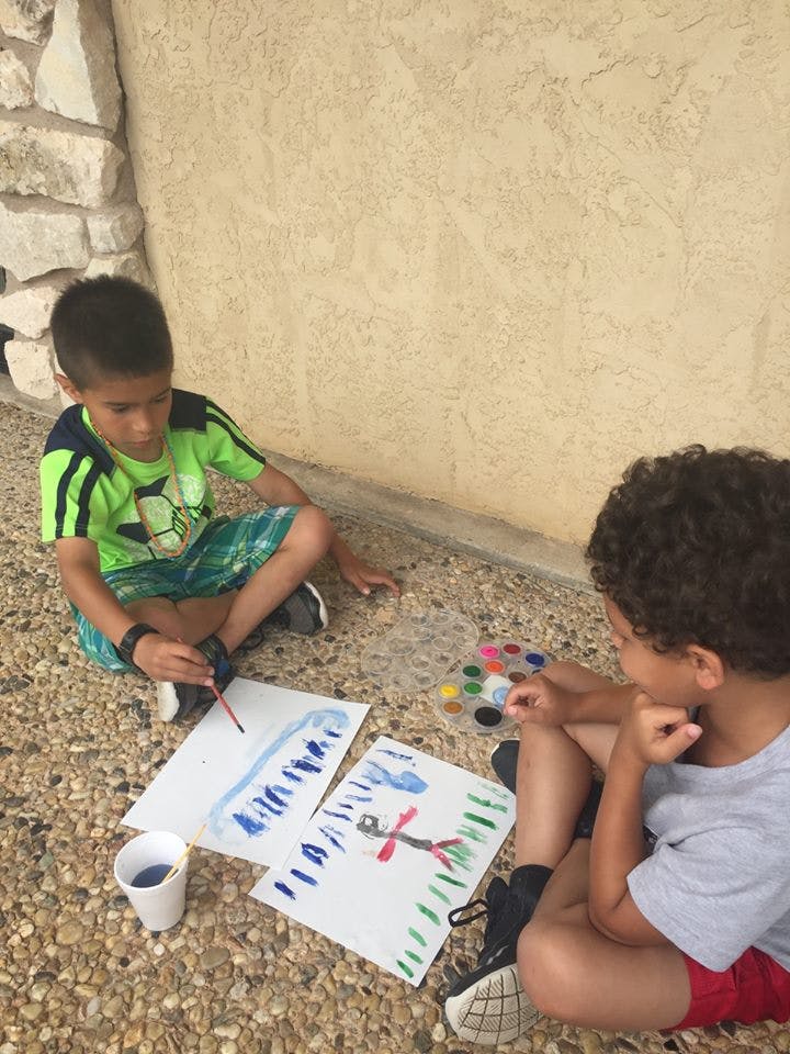Two children sitting on the ground painting with watercolors and paintings