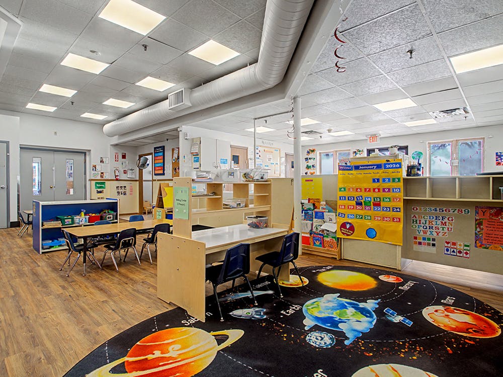 Classroom with small tables and chairs, and a round rug depicting the solar system