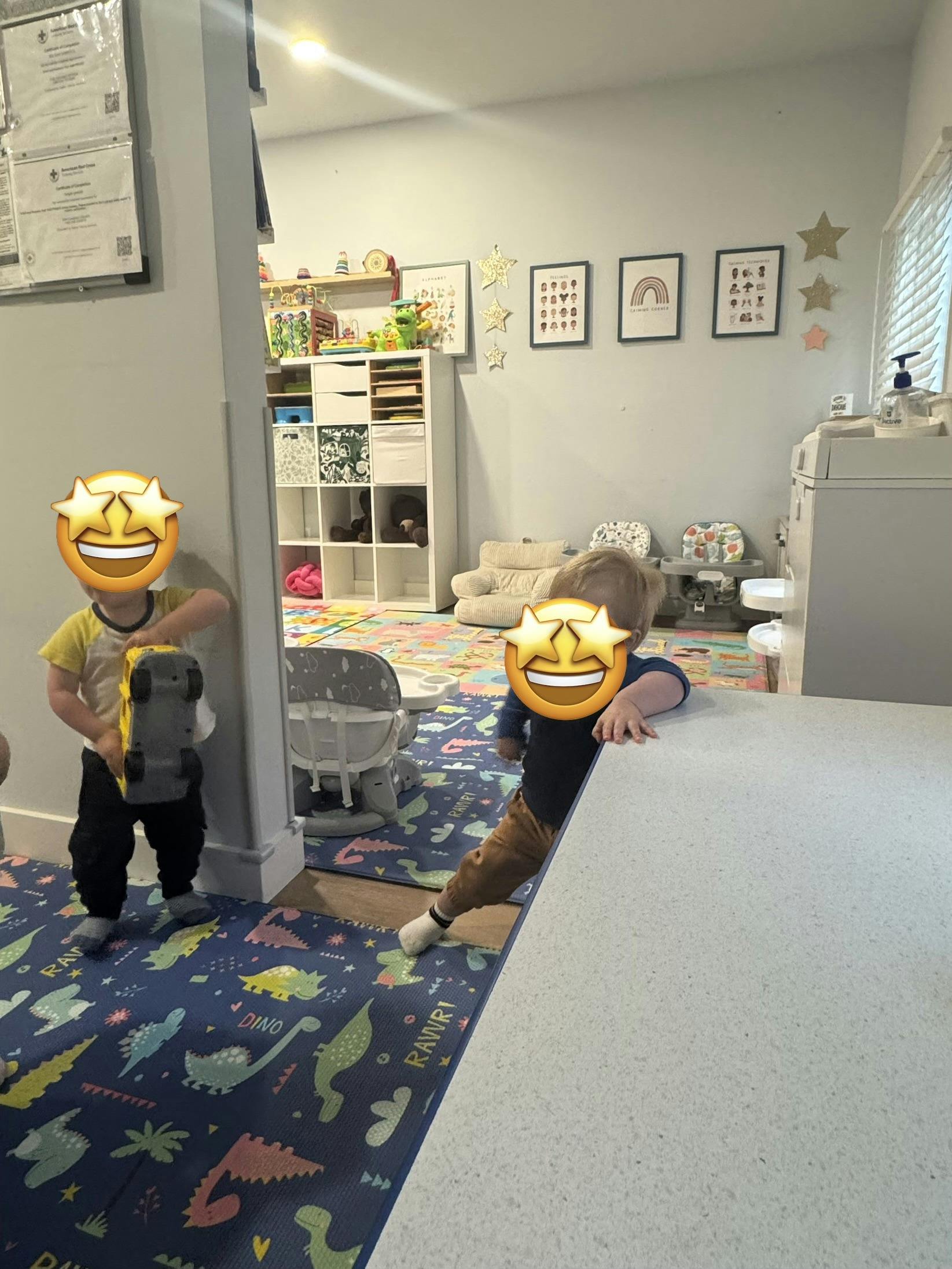 Two children playing on a dinosaur-patterned mat in a room with shelves of toys