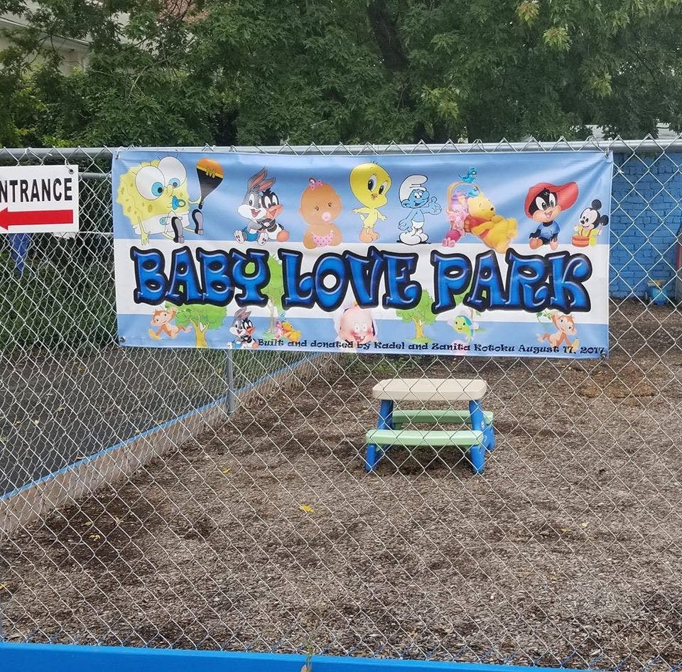 Baby Love Park banner on a chain link fence with a small bench