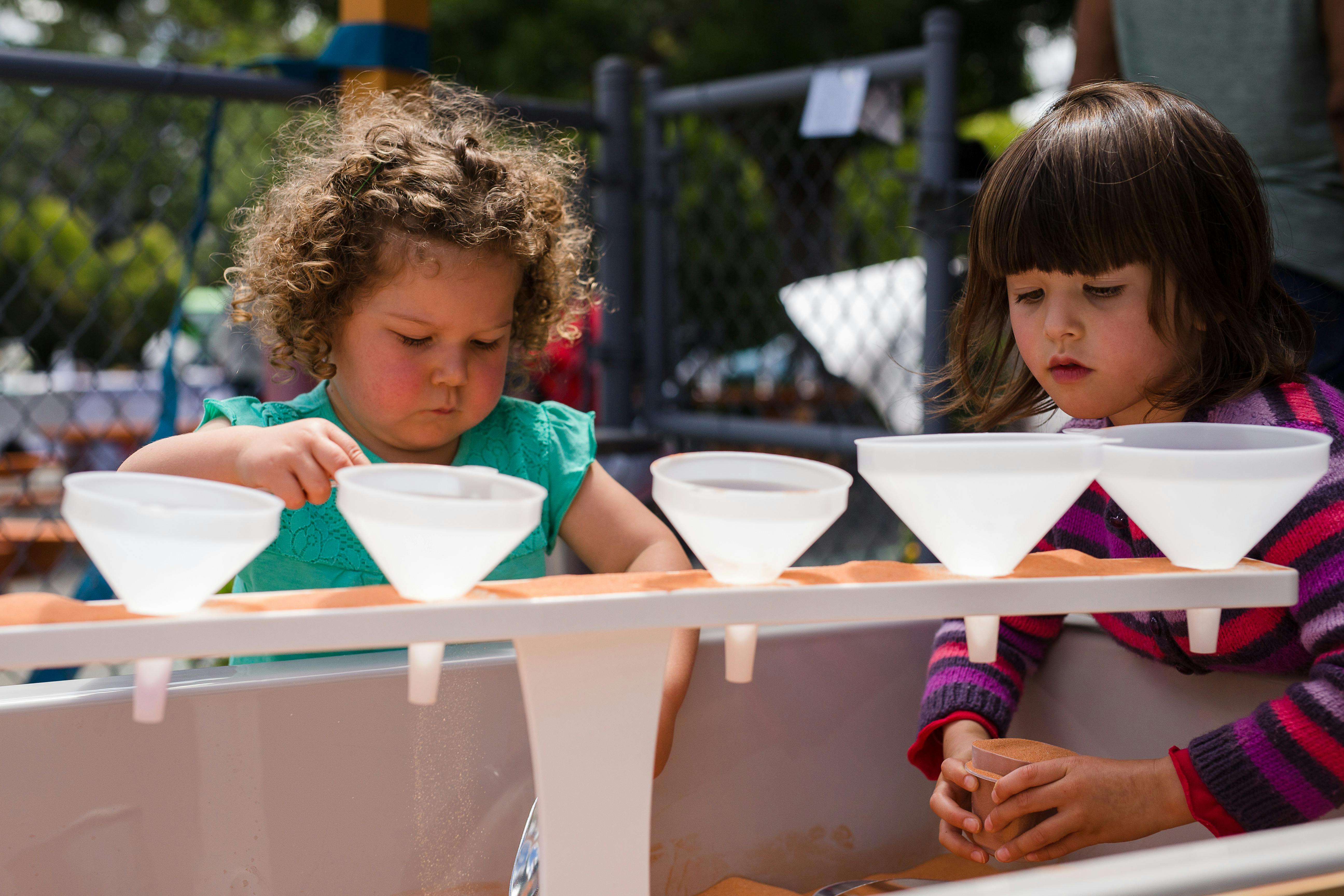 Two children playing with funnels in a water table
