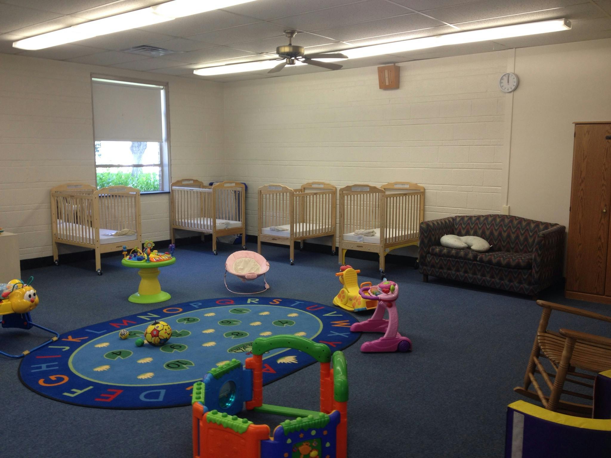 Nursery room with multiple cribs, a sofa, and a colorful play rug