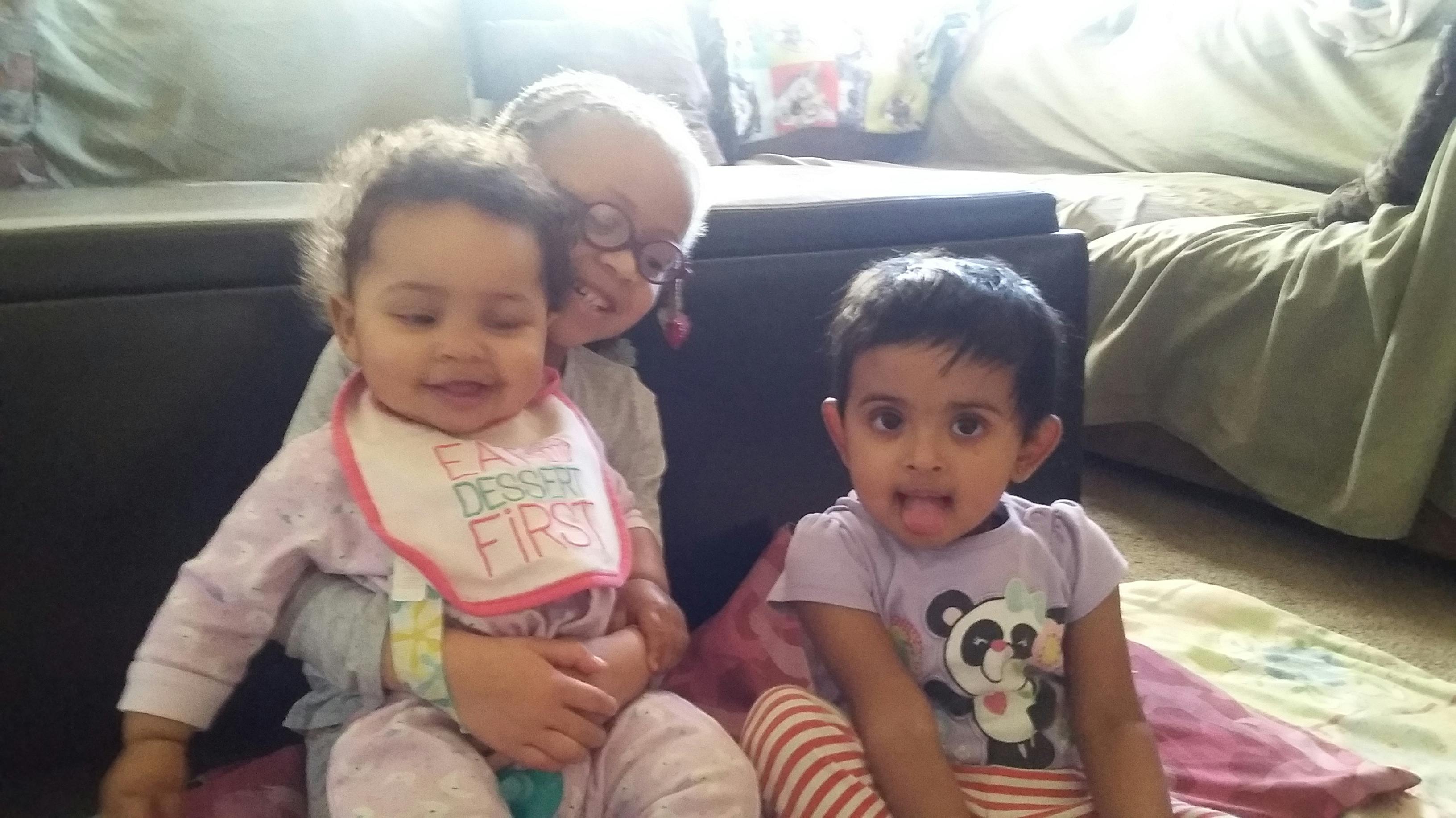 Two children sitting on a floor with a person behind them