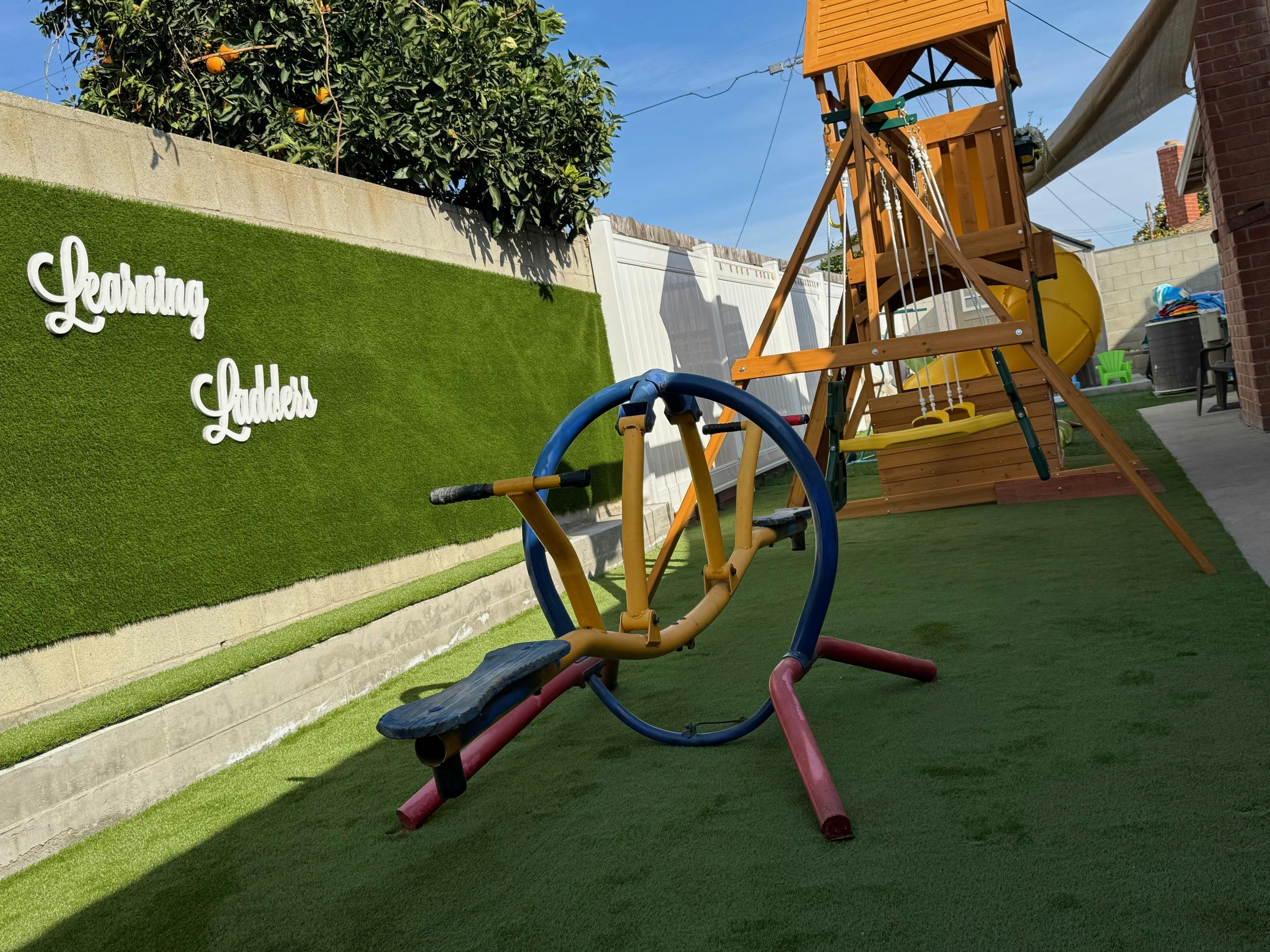 Playground with swings, slide, and a multi-person spinner on artificial turf