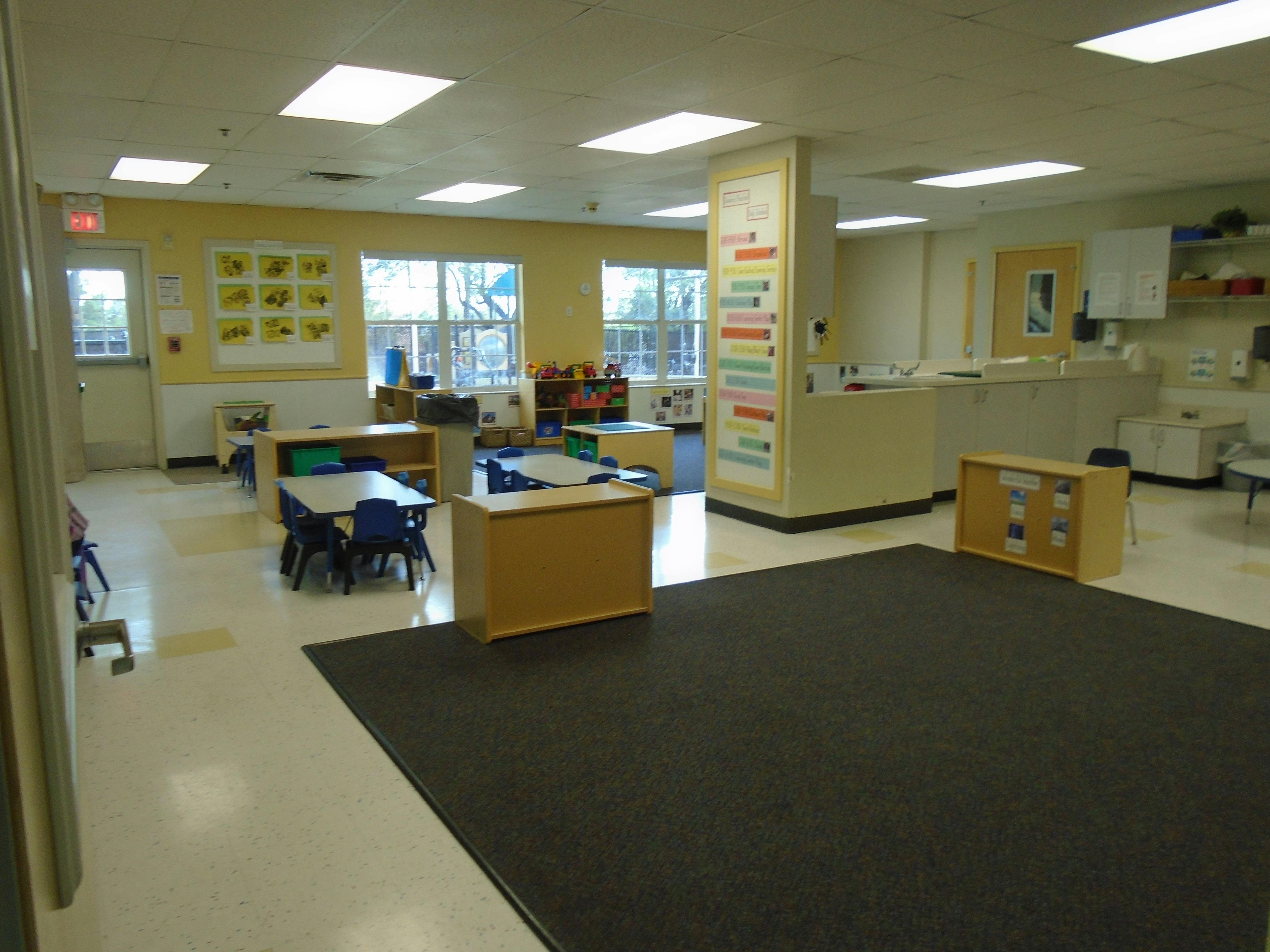 An empty classroom with small tables, chairs, and play equipment