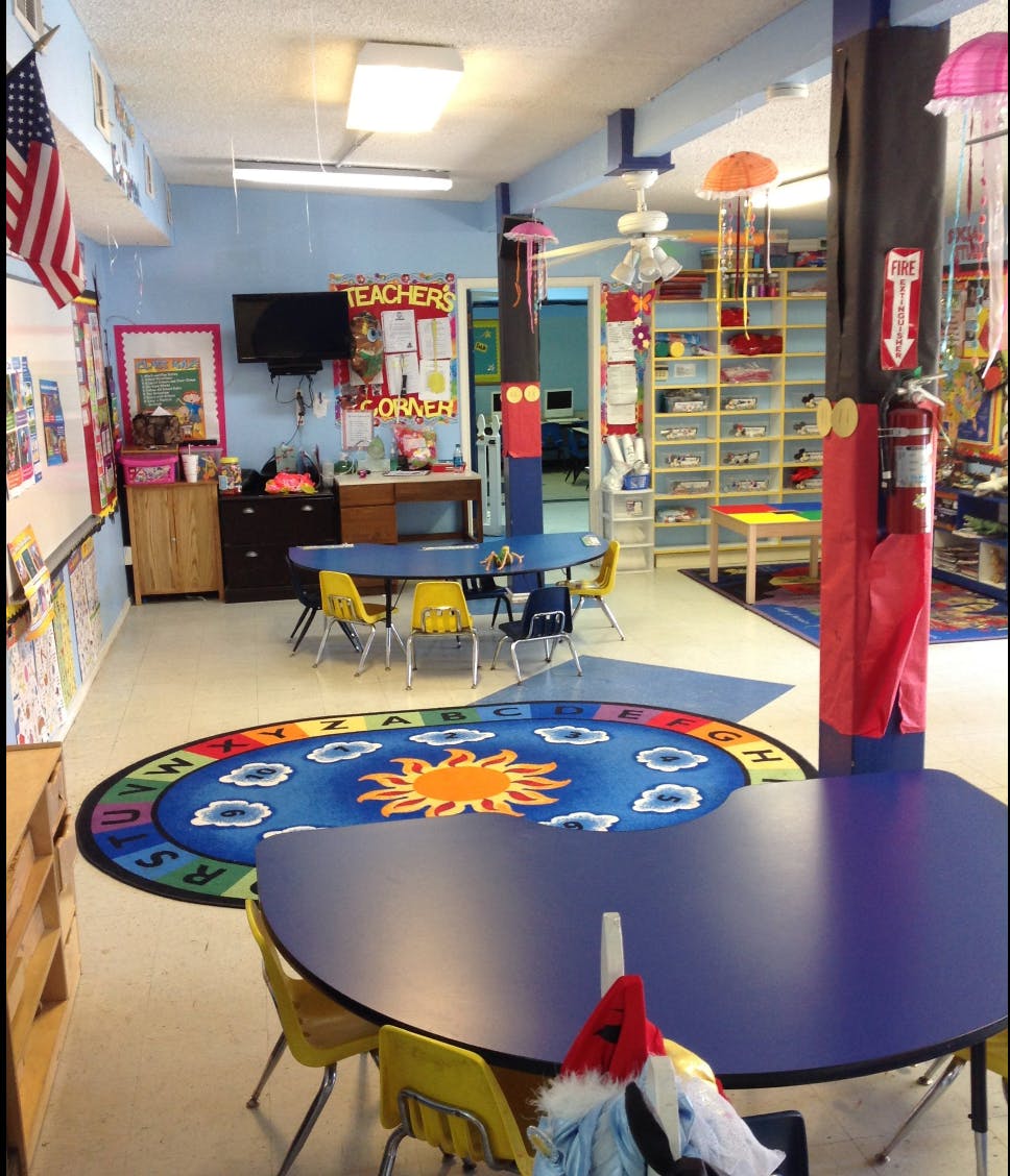 Classroom with blue tables, yellow chairs, and a sun-themed rug