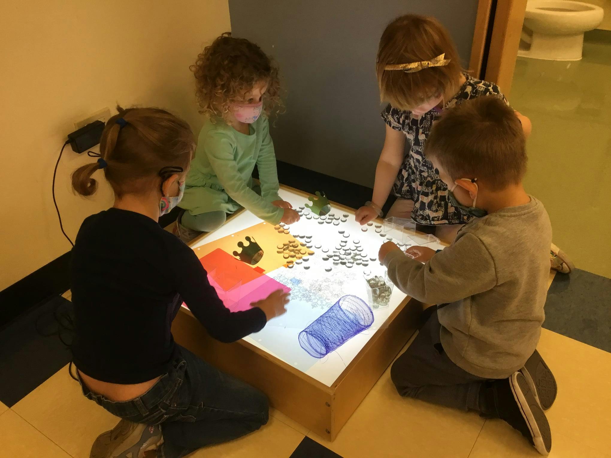 Four children playing with small objects on a light table