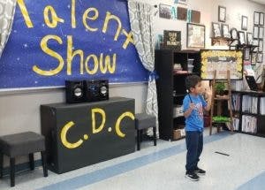 Child standing on stage in front of a "Talent Show" banner