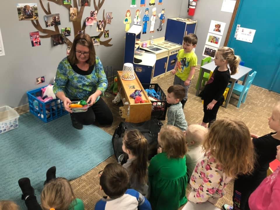 Person kneeling and showing objects to children in a classroom