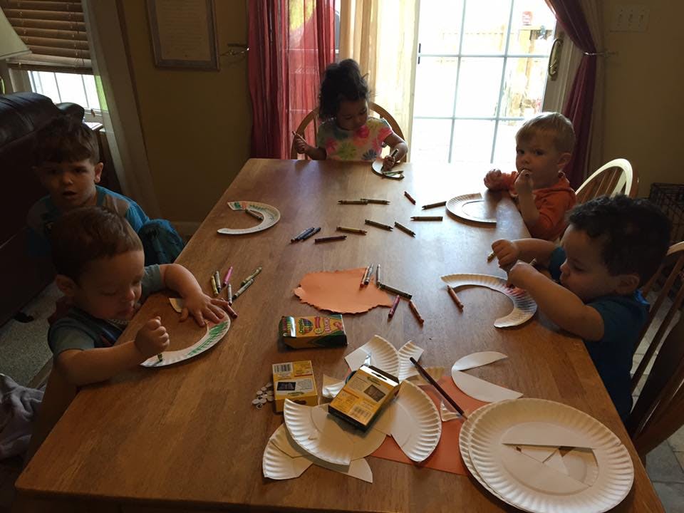 Children sitting at a table doing crafts with paper plates and crayons