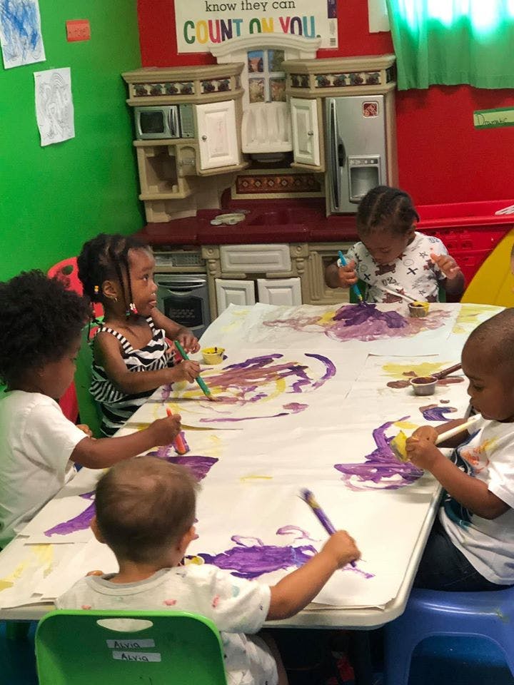Four children painting at a table in a classroom
