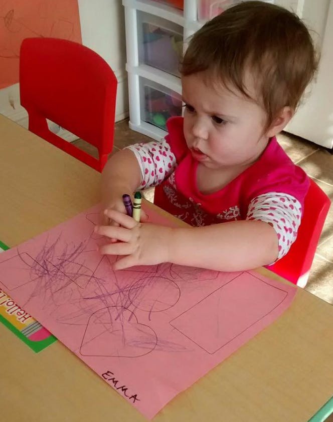 Child drawing on pink paper with crayons