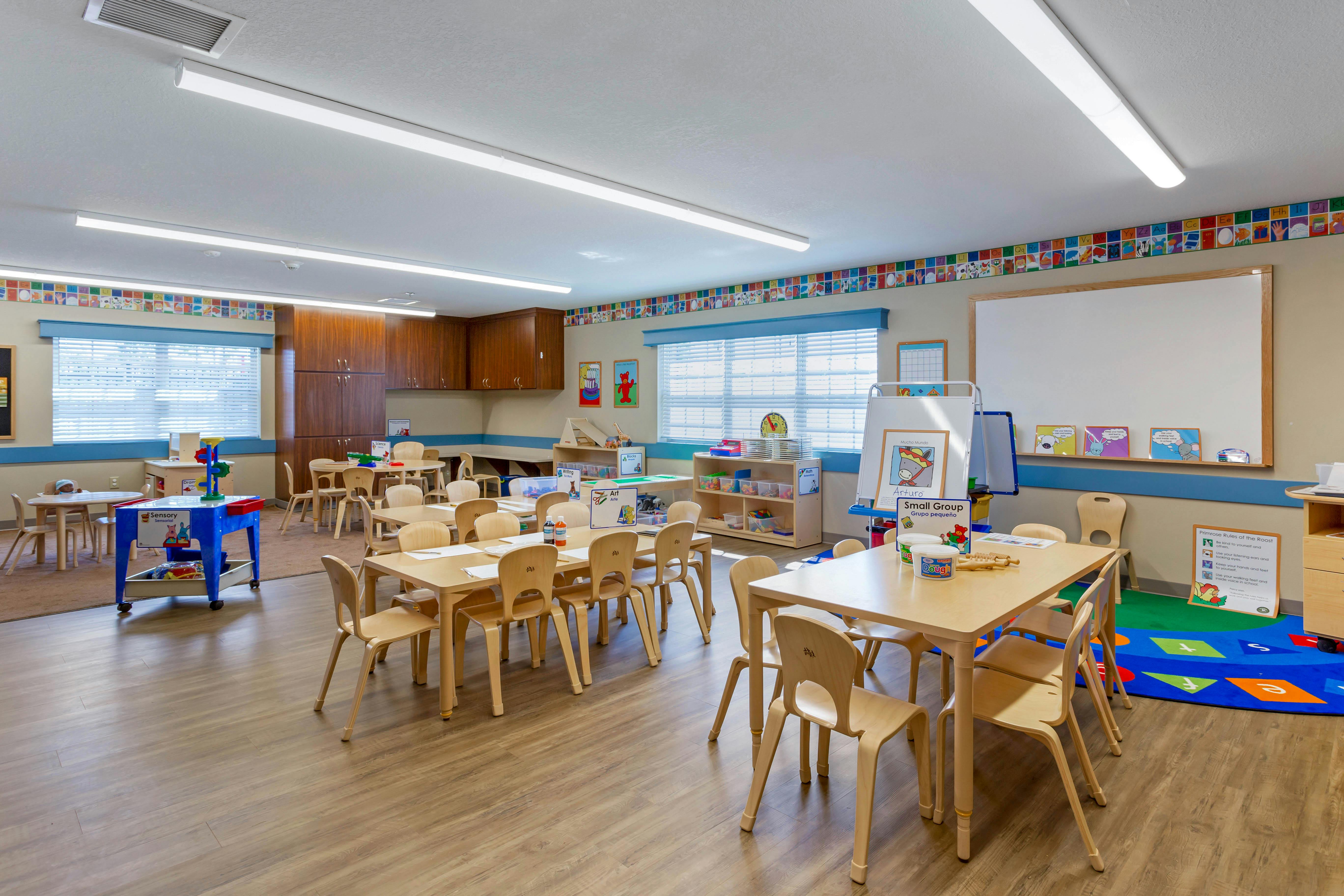 An empty early childhood classroom with multiple small tables and chairs