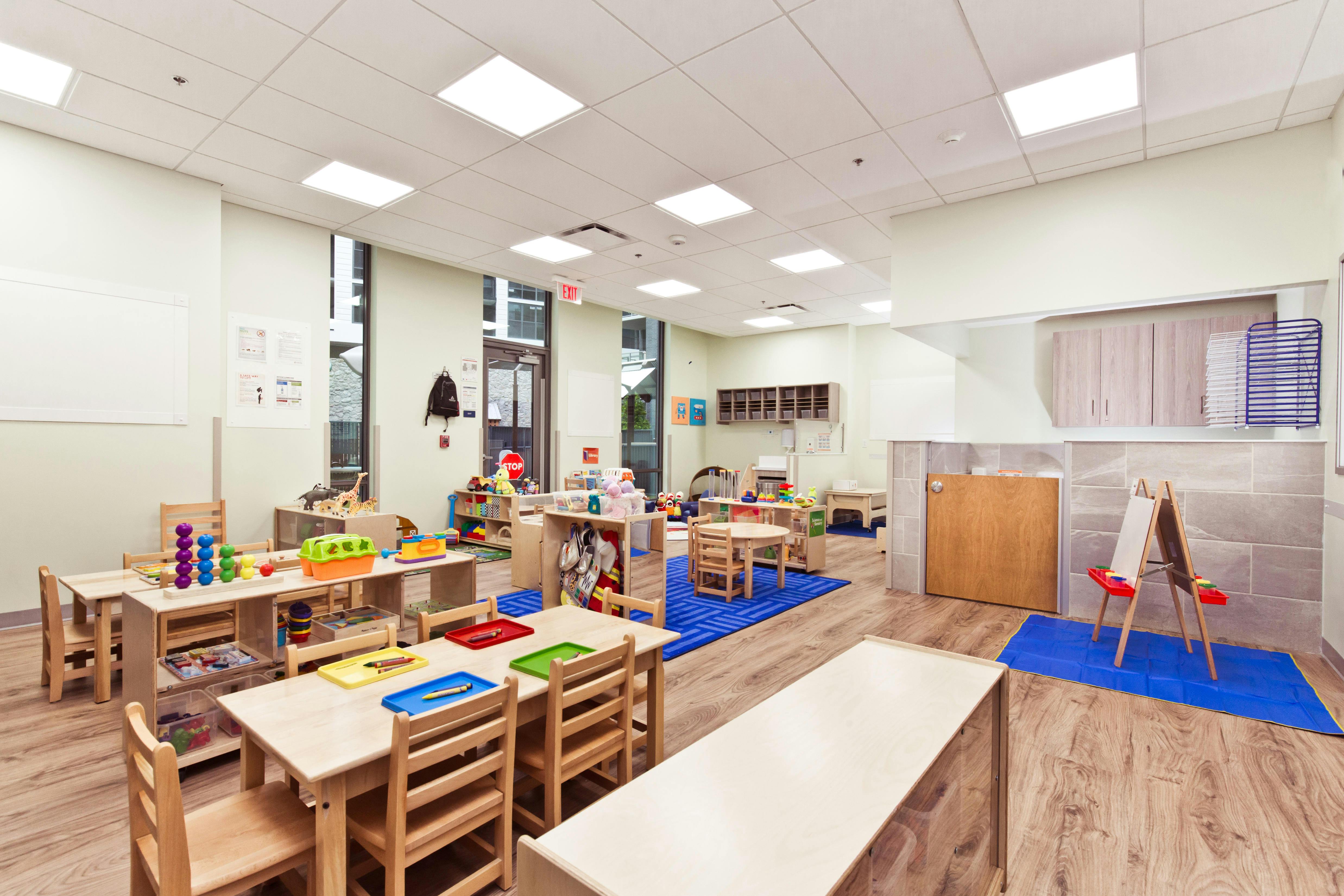 Empty classroom with small wooden tables and chairs, toys, and educational materials